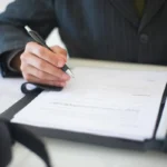 Tangan menandatangani dokumen penawaran bisnis di atas meja, menggambarkan proses finalisasi kontrak kerja sama